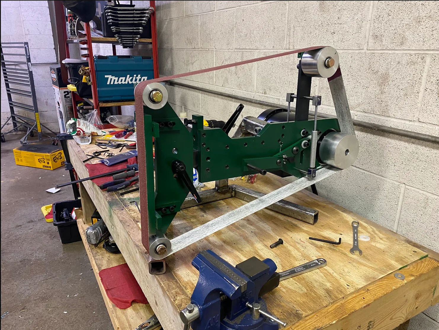 A custom-built green belt grinder on a workshop bench.